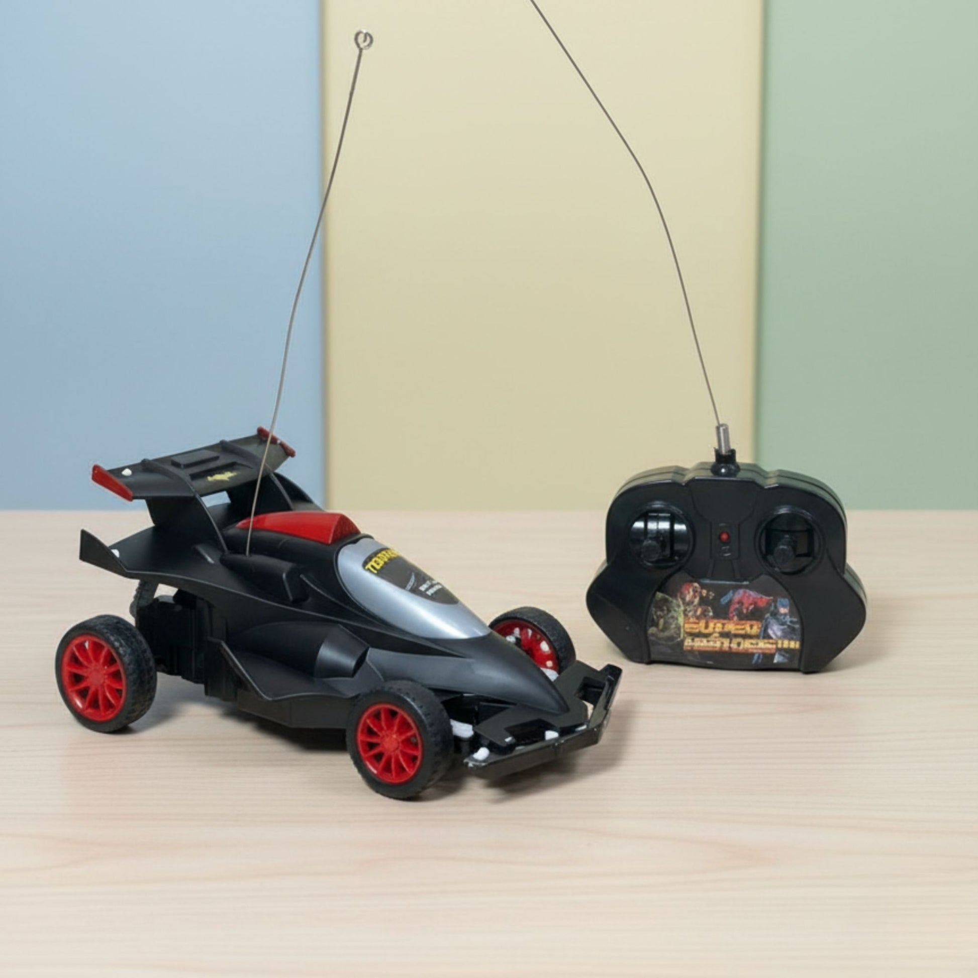 Black and red toy remote control car on a light wooden surface with a plain background