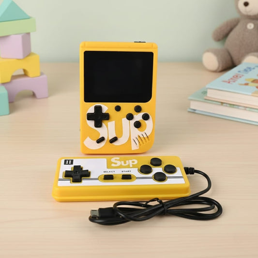 Yellow handheld gaming console with 'SUP' branding on a table with toys and books in the background - Baby Nest