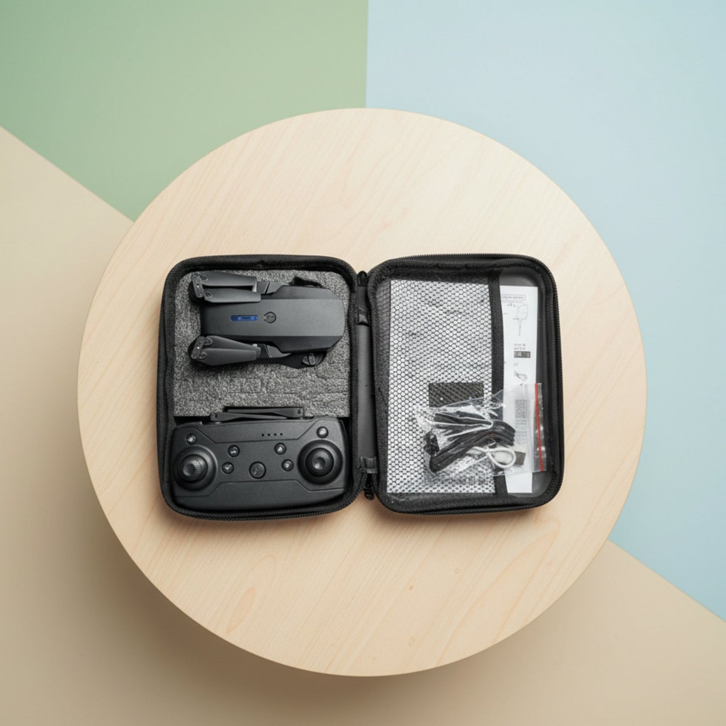 Black drone and accessories in a carrying case on a round wooden table with a colorful background